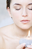 Young woman holding candle, eyes closed, cropped view