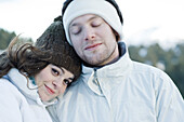 Young couple in ski clothes, young woman resting head on boyfriend's shoulder