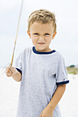 Young boy holding up stick, squinting at camera