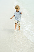 Little boy splashing in surf on beach, full length