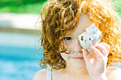Little girl holding seashell in front of face, looking at camera