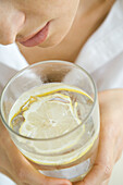 Woman holding glass of water with floating lemon slice, close-up, cropped