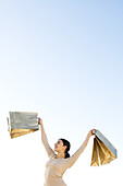 Woman holding up shopping bags, smiling, low angle view