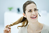 Young woman twirling her hair, wearing headset and looking away, smiling