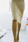 Woman wearing skirt walking barefoot across room, low section