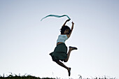 Carefree young woman leaping, scarf in hand trailing behind