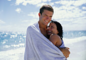 Couple embracing at beach, wrapped in towel, portrait