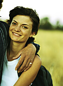 Woman with man's arm around her smiling at camera, portrait