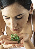 Woman holding sprig of basil in palms, eyes lowered, close-up