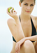 Young woman in bikini holding apple, looking at camera