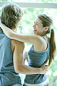 Young couple in exercise clothing standing with arms around each other, woman laughing
