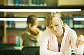 Female college student sitting at table in library, studying