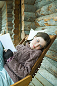 Teenage girl reading book, smiling at camera, dressed in winter clothing