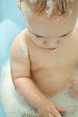 Naked baby sitting in bathtub, looking down, waist up
