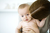 Woman kissing baby's cheek, baby looking at camera