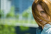 Young red haired woman with hair blowing across face, portrait