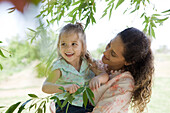 Mother holding young daughter outdoors, girl holding onto tree branch