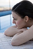 Woman lying beside pool with head resting on arms, cropped
