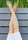 Woman sitting on deck, legs crossed at ankles, cropped view of legs
