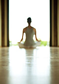 Yoga class, woman sitting in lotus position, defocused and backlit