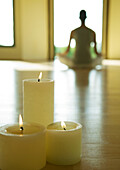 Yogaklasse, brennende Kerzen, während die Person im Lotussitz im unscharfen Hintergrund sitzt