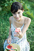 Young woman holding up piece of watermelon, smiling at camera