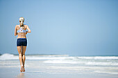 Young woman running on beach, rear view