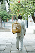 Elderly man in traditional Chinese clothing, carrying bird cage over back, rear view