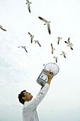 Man releasing bird outdoors, open cage in hand