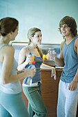 Young adults wearing exercise clothes, standing in cafeteria, having healthy snack and chatting