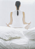 Woman sitting in lotus position on bed, rear view, blurred