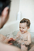 Toddler boy splashing in bath with his father