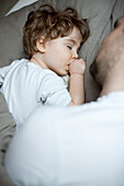 Toddler boy sleeping beside father, cropped