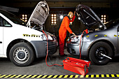 A crash test dummy using jumper cables with two cars