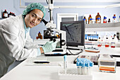 A lab technician using a microscope, looking at camera