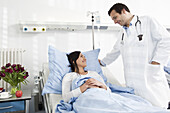 A doctor talking to a smiling patient lying in a hospital bed