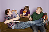 Two teenage boys eating pizza while another watches enviously
