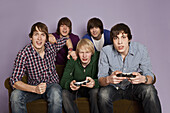 Two teenage boys playing a video game while their friends cheer them on