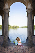 Two children sitting together under an arch next to a lake