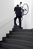 Businessman returns home carrying his bicycle up steps