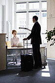 A traveling businessman talking to a businesswoman sitting at a desk