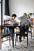 A hip mixed aged couple reading newspapers and having breakfast