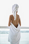 Woman wrapped in towel looking at sea view from balcony