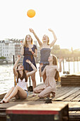 Four female friends tossing a ball around on a jetty next to Spree River, Berlin, Germany