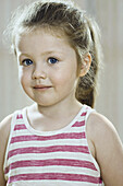 A young girl wearing a striped tank top and looking shyly into the camera