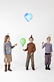 Three kids wearing party hats and holding balloons