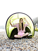 A young woman sitting in a beach tent on a rocky beach