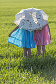 Twin sisters standing in a sunny field under an umbrella