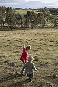 A girl holding hands with a young boy and walking in nature