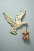 A plastic bird carrying a sack in its beak, hanging on wall